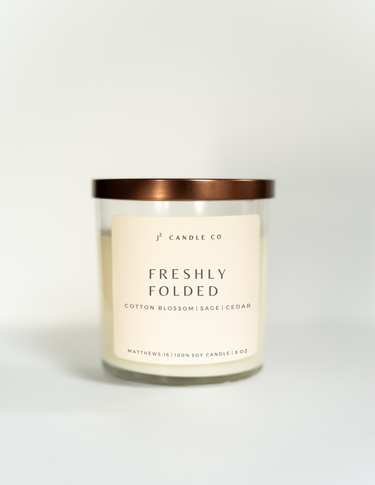 Freshly Folded soy candle with Cotton Blossom, Sage, Cedar, clear glass jar with bronze lid.