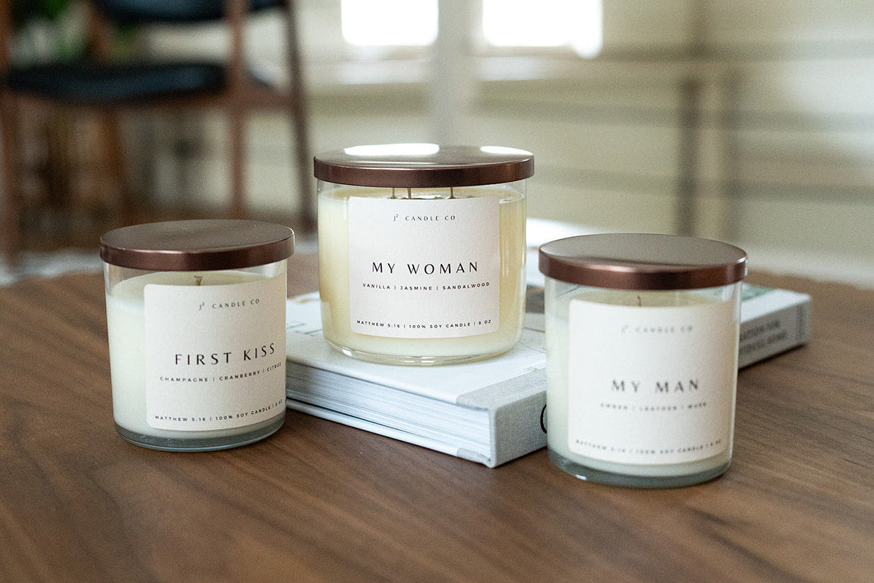 Three candles labeled 'First Kiss', 'My Woman', and 'My Man' on a wooden surface.